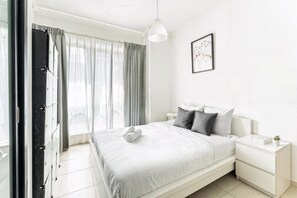 A modern bedroom with a bed, bedside tables, a hanging light, and a window with curtains. - HAVN - 1 bedroom in Dubai Marina with Marina Views (Dubai)