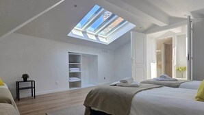 A bedroom with a skylight, a wardrobe, a bed, and a small table with a plant.