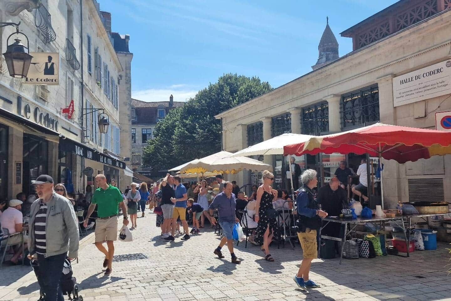 Una calle animada con peatones, mesas al aire libre y puestos de mercado.