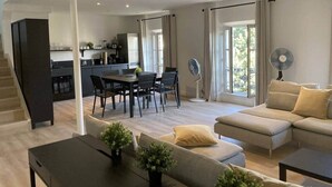 A modern living room with a sofa, a dining table, and chairs. There is a staircase leading to another level.