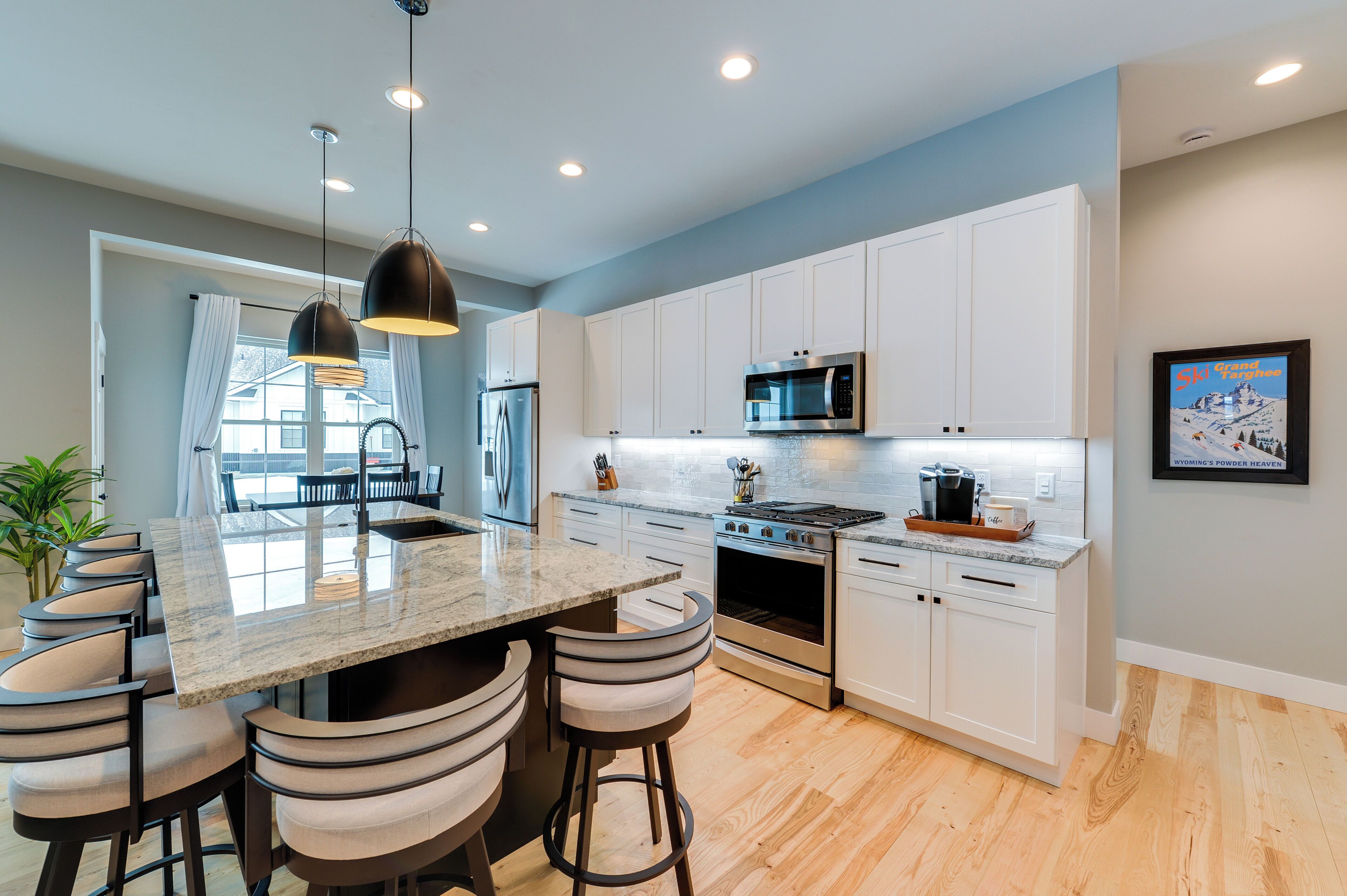 Una cocina moderna con armarios blancos, electrodomésticos de acero inoxidable y una isla central con taburetes de bar.