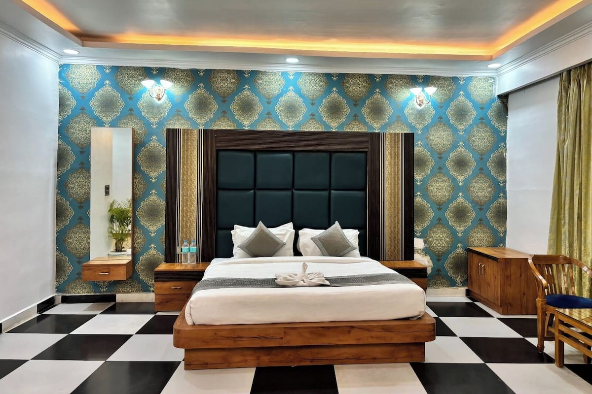 Quarto de hotel com chão xadrez, uma cama grande com cabeceira escura e papel de parede estampado.