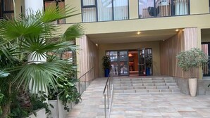 L’entrée d’un hôtel, avec un sol carrelé, un escalier menant à l’entrée et des plantes en pot de chaque côté.