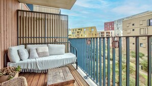 En balkon med trægulv, hvid sofa med puder og en fletstol.