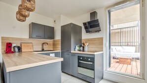 Et moderne køkken med grå skabe, en træbordplade, et indbygget ovn og et stort vindue med udsigt til en balkon.