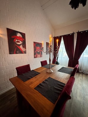 Un espace repas avec une table en bois, des chaises rouges, des murs en briques blanches et des œuvres d’art.