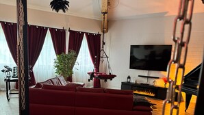 A living room with a red sofa, a hanging chair, a TV, a fireplace, and a plant. - Red Silence I Design Suite near Koblenz I Experience, Not Standard (Bendorf)