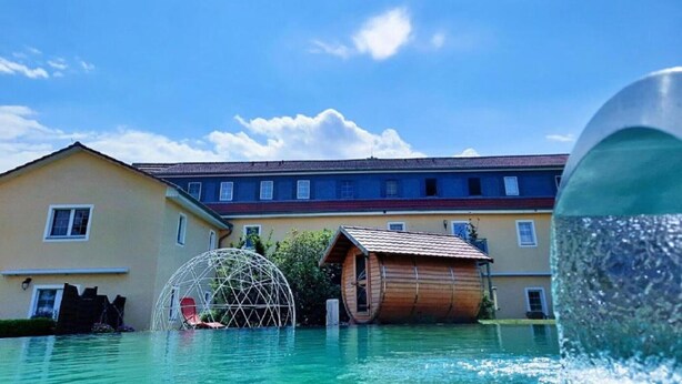 Une piscine dotée d’un dôme géodésique et d’une structure en forme de tonneau en bois, entourée de bâtiments.