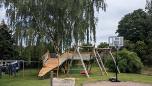 Une aire de jeux avec un toboggan en bois, un filet d’escalade et un panier de basket.