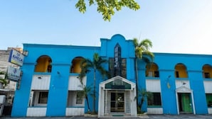 Un bâtiment bleu avec une entrée centrale, de nombreuses fenêtres en arc de cercle et un panneau indicateur sur le côté gauche.
