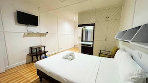 Une chambre d’hôtel comprenant un lit, un téléviseur fixé au mur, un miroir et une armoire ornée d’un motif géométrique.