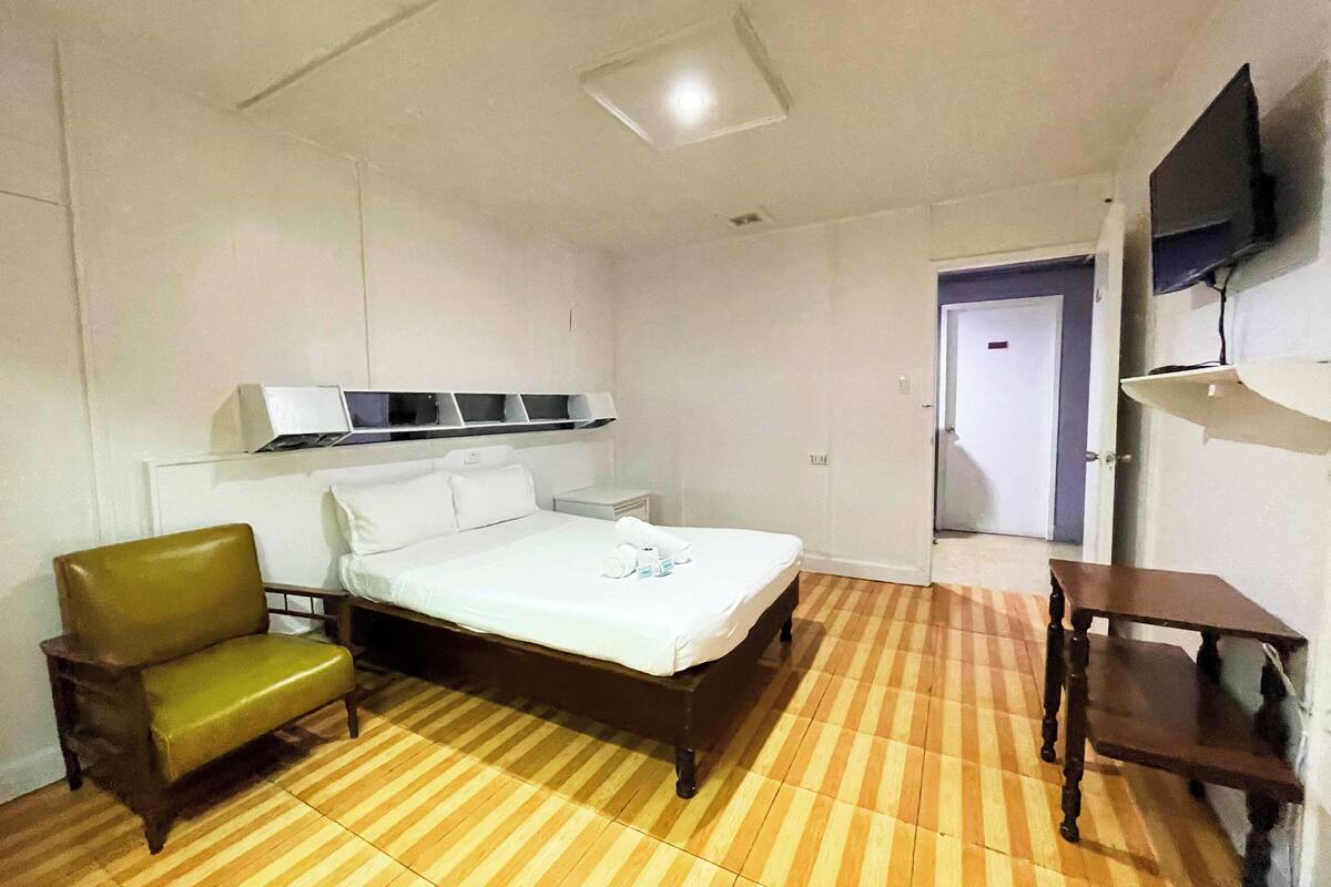 A hotel room with a bed, a chair, a TV on the wall, and a door leading to another room.