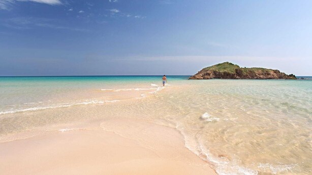 Ein Strand mit klarem türkisblauem Wasser und sandigem Ufer.