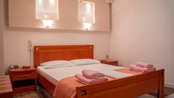 Une chambre à coucher avec un lit en bois, des oreillers blancs, une couverture rose et deux lampes fixées au mur.