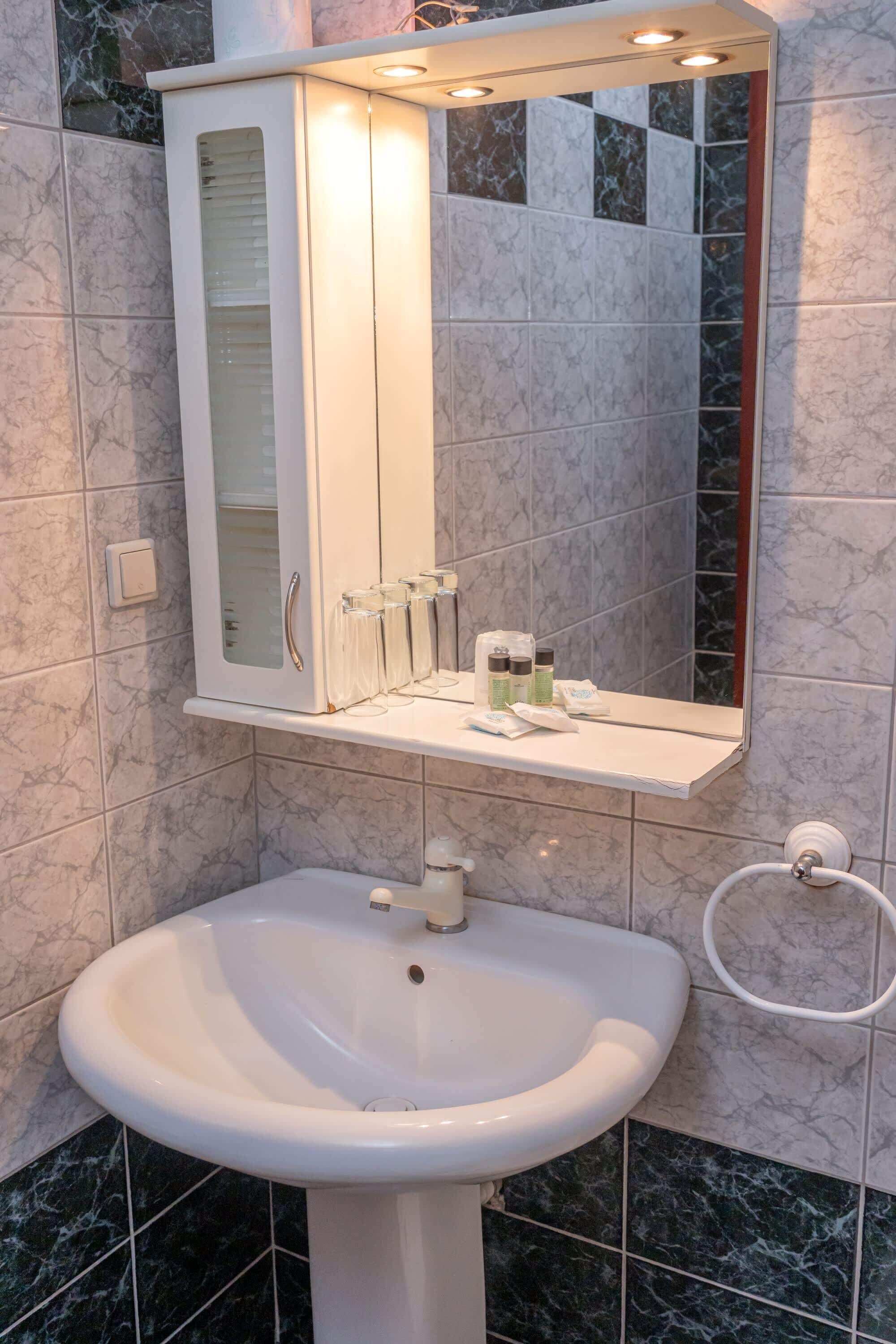Un bagno con un lavabo a colonna bianco, un pensile a specchio e articoli da toilette sul ripiano.