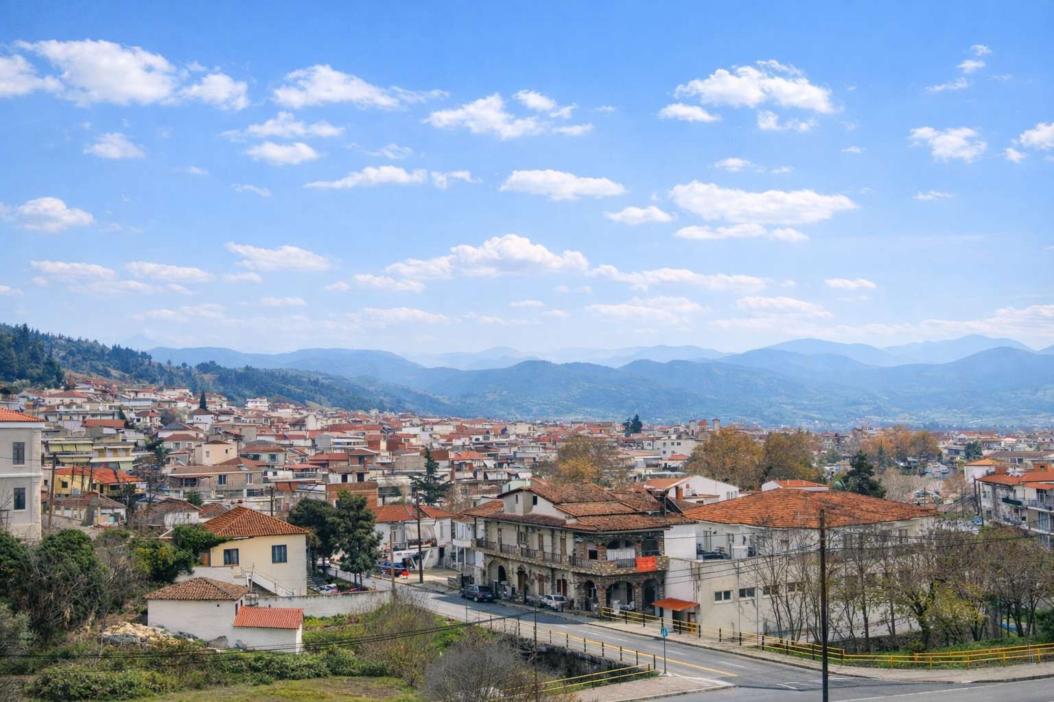 A town with red-tiled roofs, a mix of old and new buildings, and a view of distant mountains under a clear sky.