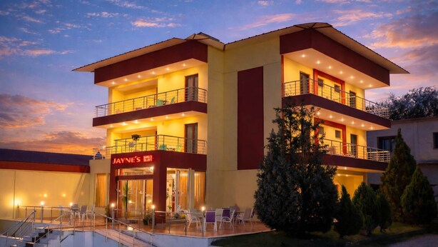 Ein mehrstöckiges Hotel mit roter und gelber Fassade, einem gut sichtbaren Eingang und einer Außenbereich-Sitzgelegenheit.
