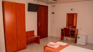 Ein Hotelzimmer mit Bett, Schreibtisch, Stuhl, Kleiderschrank und kleinem Kühlschrank.