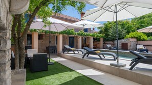 A poolside area with lounge chairs, umbrellas, and a stone building in the background. - Villa Katarina by Villas Guide (Barban)