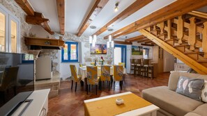 A rustic interior with exposed wooden beams, a dining area with yellow chairs, a kitchen with a stone wall, and a staircase. - Villa Katarina by Villas Guide (Barban)