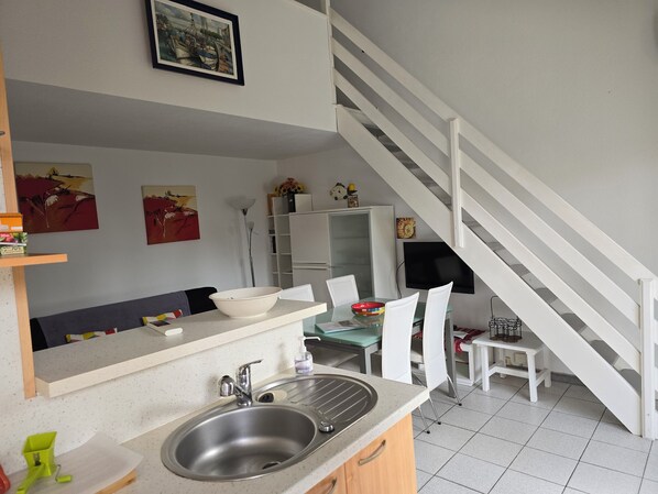 A modern kitchen with a sink, white chairs, and a staircase.
