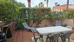 Eine Terrasse mit Holzboden, einem weißen Tisch und grauen Stühlen.