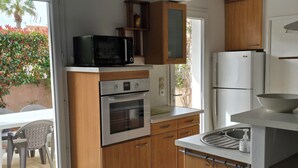 Eine kompakte Küche mit Holzausstattung, einer eingebauten Mikrowelle, einem Backofen, einem Kühlschrank und einer kleinen Essecke mit Tisch und Stühlen.
