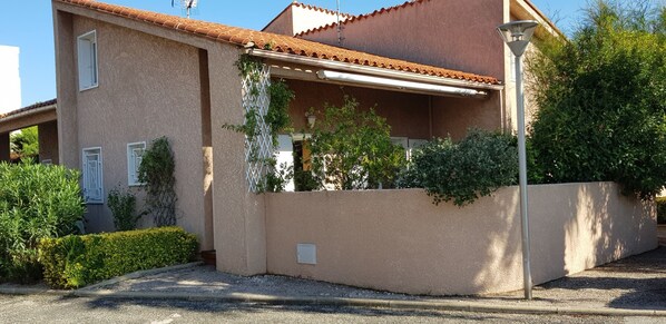 A two-story house with a tiled roof, a covered porch, and a small garden area with shrubs and a tree. - 3* house near port and beach (Saint-Cyprien)