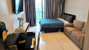 A hotel room with a bed, a sofa, a desk with a computer, a fan, and a TV. - Budget Studio Condo With Resort-style Pool - Laguna Beach Resort 1, Jomtien (Pattaya)