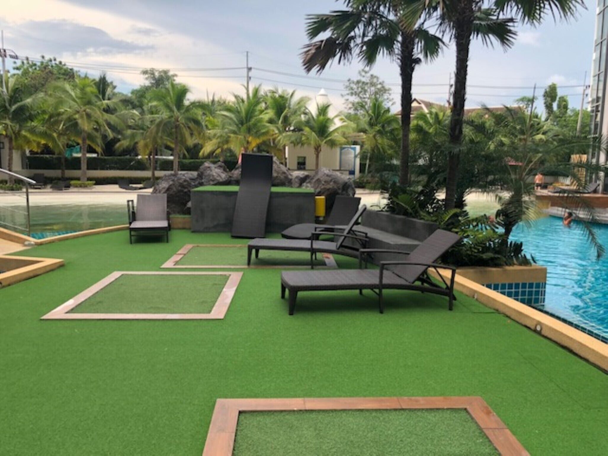 A poolside area with artificial grass, lounge chairs, and a pool.