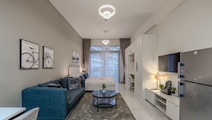 Ett modernt och väl upplyst vardagsrum med en soffa, ett soffbord och en säng. På väggen hänger inramade tavlor, och det finns också en tv och ett kylskåp.