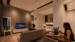 Un soggiorno moderno con divano, tavolo da pranzo con sedie, televisore a schermo piatto e vista sulla città.