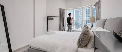 Une chambre d’hôtel moderne avec un grand lit, une table de chevet, une lampe et une vue sur le paysage urbain grâce à une grande fenêtre.