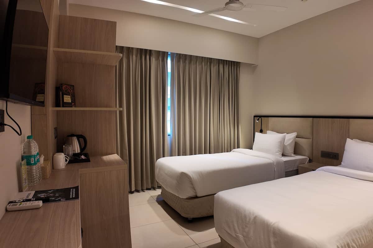 Habitación de hotel con dos camas, un escritorio con cafetera, televisor y ventana con cortinas.