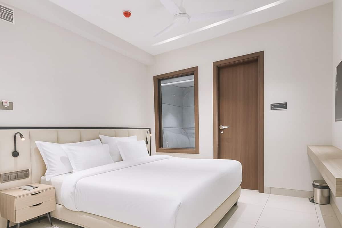 Una habitación de hotel moderna con una cama grande, una mesita de noche, un armario y un pequeño cubo de basura.