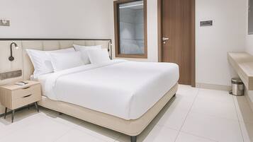 A modern hotel bedroom with a large bed, a nightstand, a wardrobe, and a bathroom area.