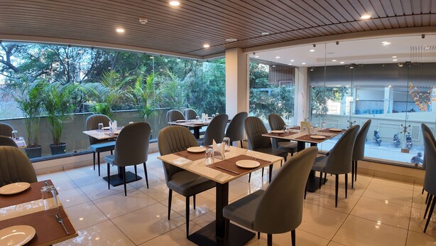 A restaurant with tables set for dining, chairs, and potted plants. - Aarambh by The Sky Imperial Indore (Indore)