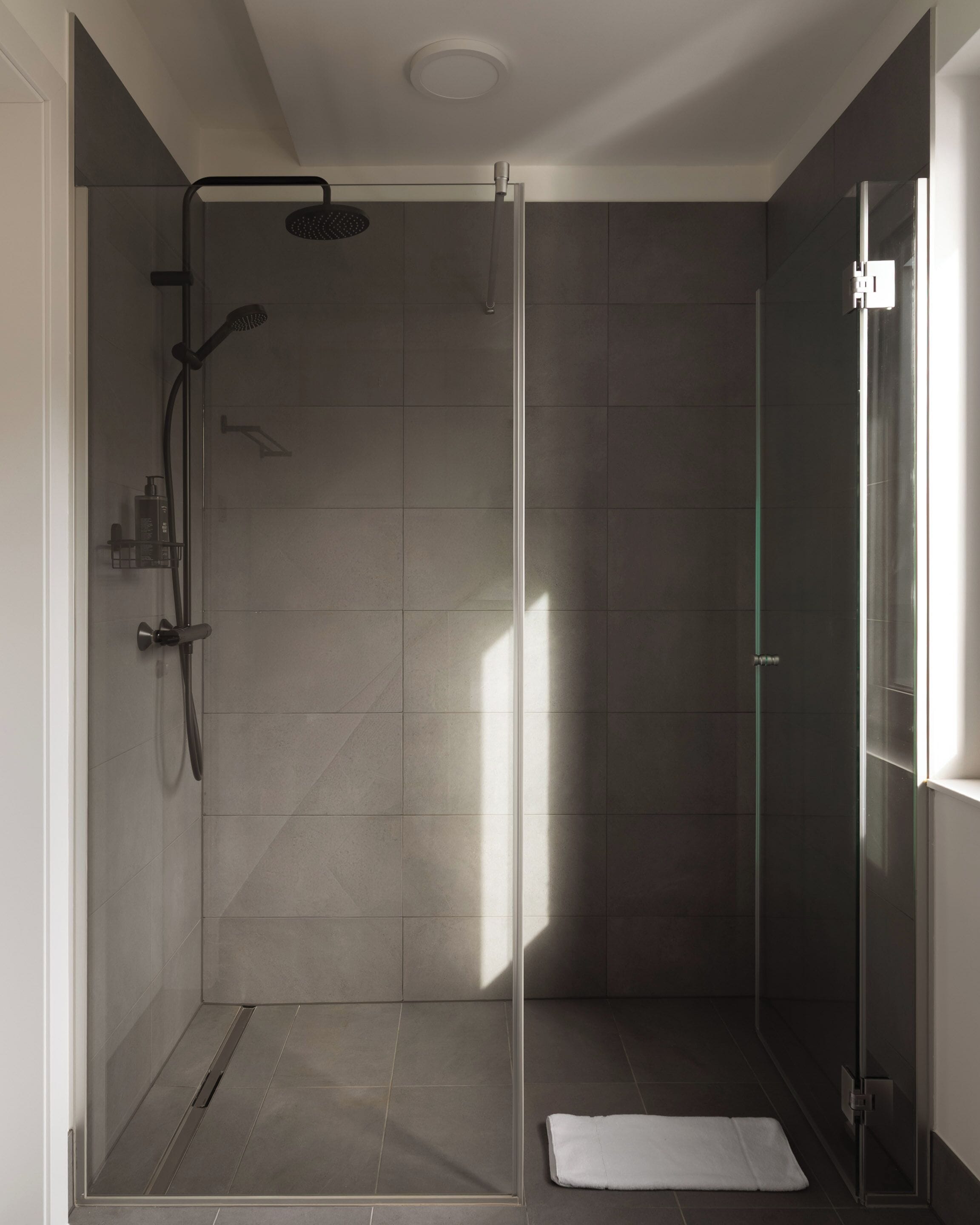 A modern shower with a glass door, a handheld showerhead, and a wall-mounted faucet.