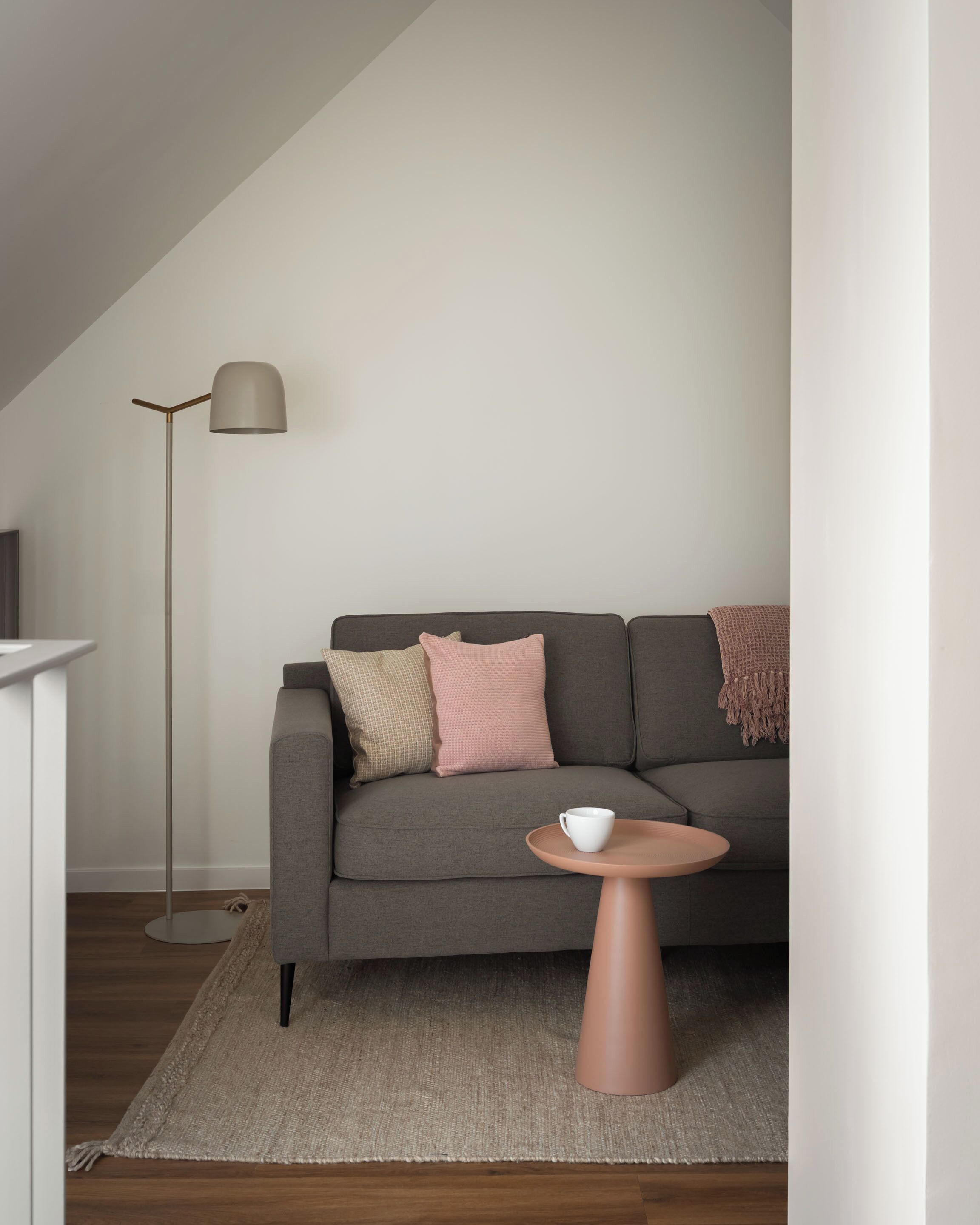 Un salon moderne avec un canapé gris, une petite table ronde sur laquelle se trouve une tasse blanche, et un lampadaire.