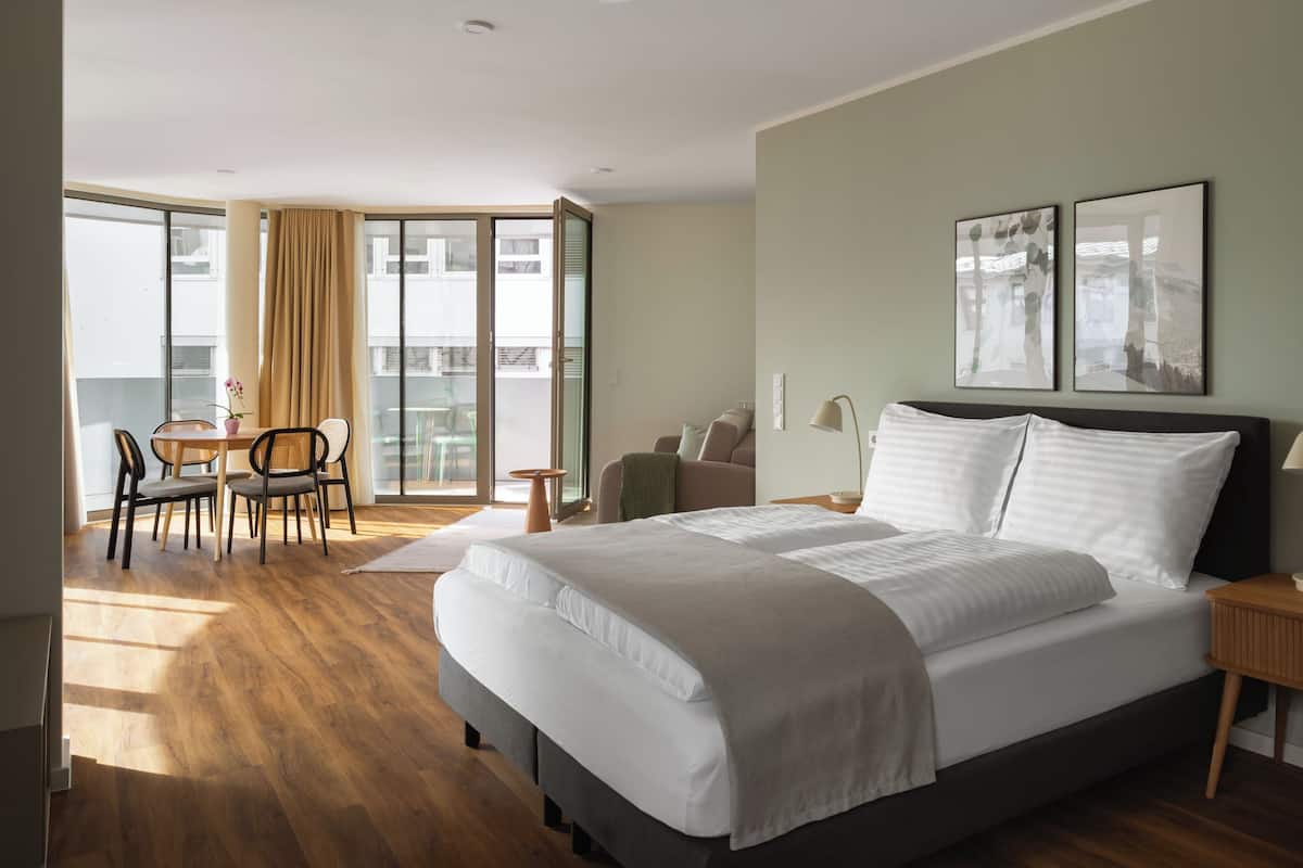 Ein Hotelzimmer mit einem großen Bett, einem Schreibtisch mit Stühlen, einem Balkon mit Tisch und Stühlen sowie zwei gerahmten Bildern an der Wand.