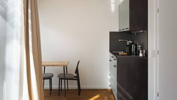 A compact room with a bed, a small table with two chairs, a kitchenette, and a window with curtains.