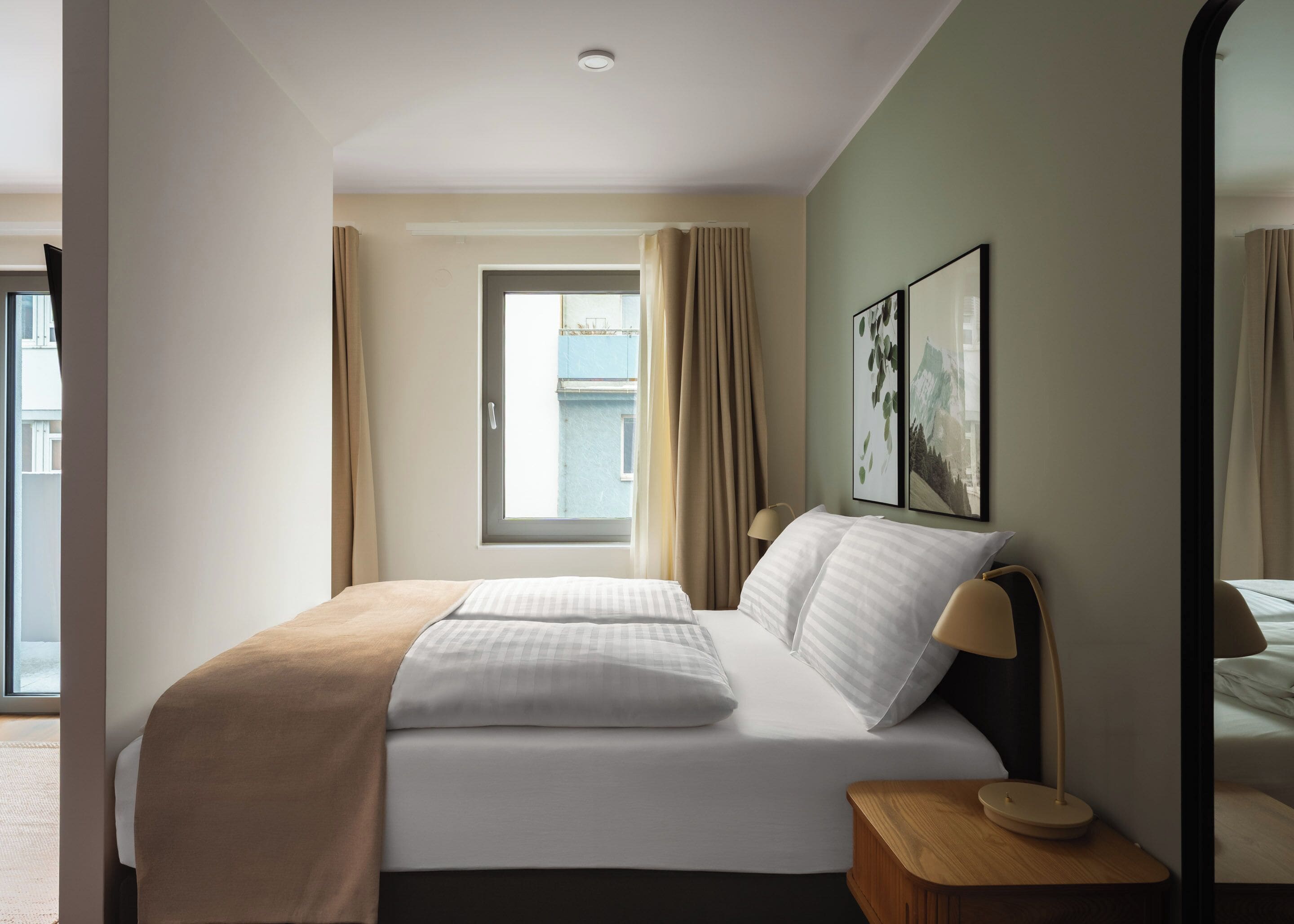 Een hotelkamer met een bed, nachtkastje, spiegel en raam met gordijnen.