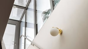 Una escalera moderna con escalones de madera, techo de cristal y una lámpara fijada a la pared.