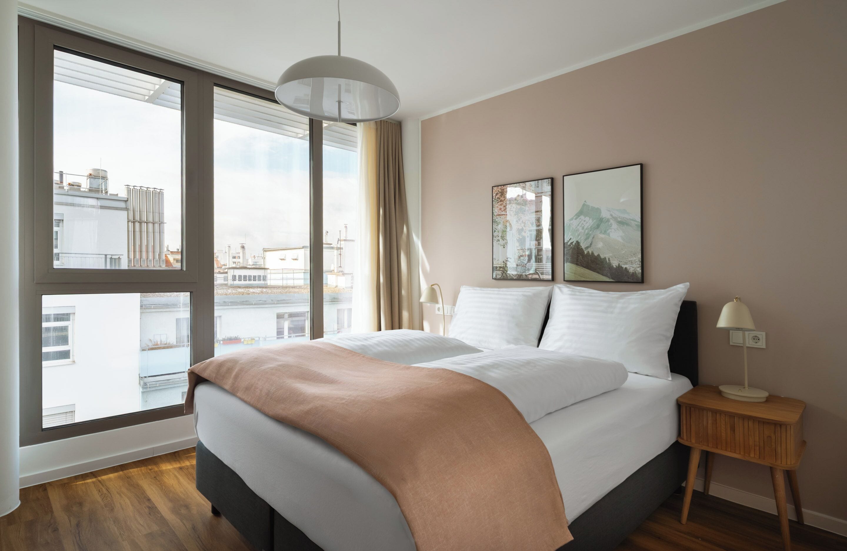 A modern hotel room with a large bed, a nightstand, a lamp, and two framed pictures on the wall.