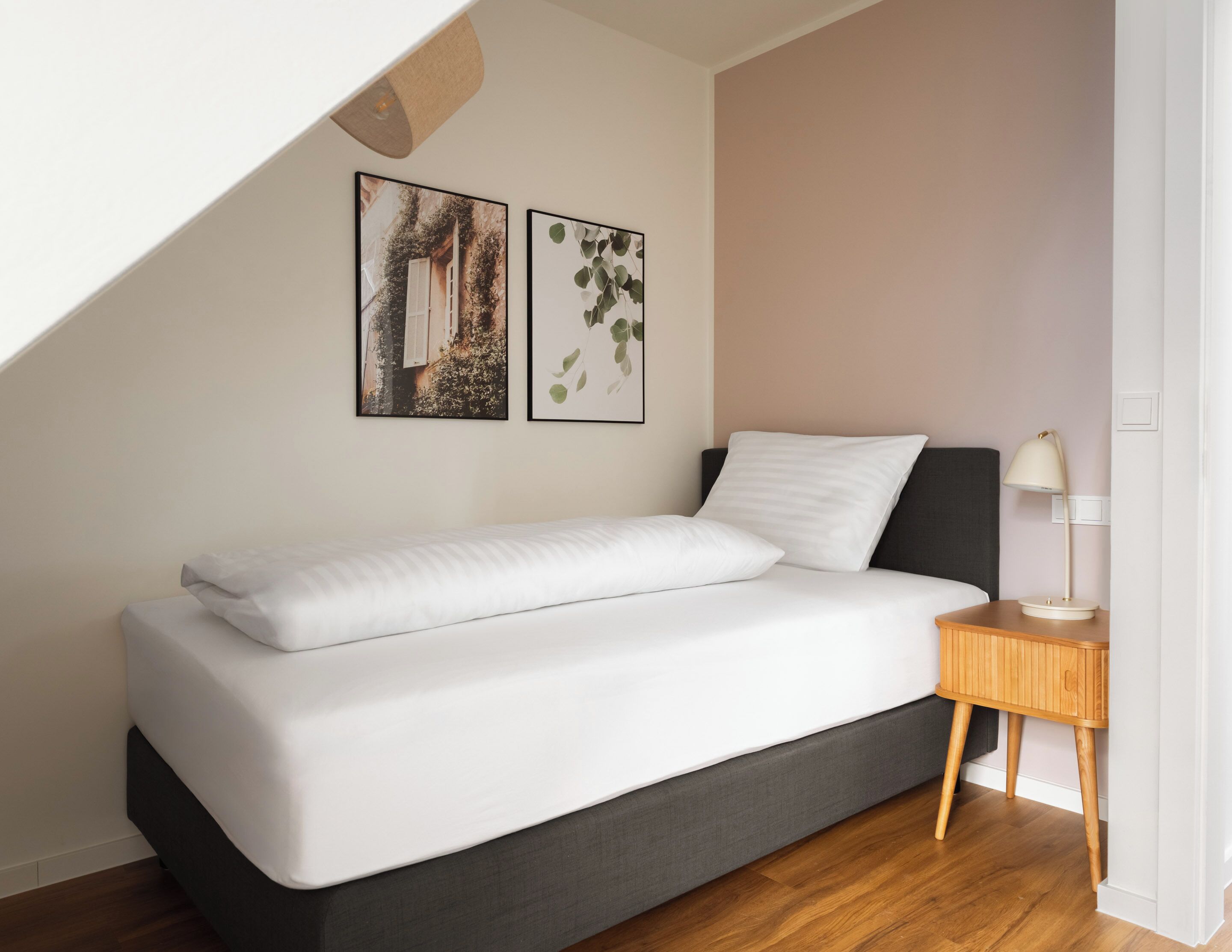 A modern bedroom with a bed, a nightstand, and two wall-mounted pictures.