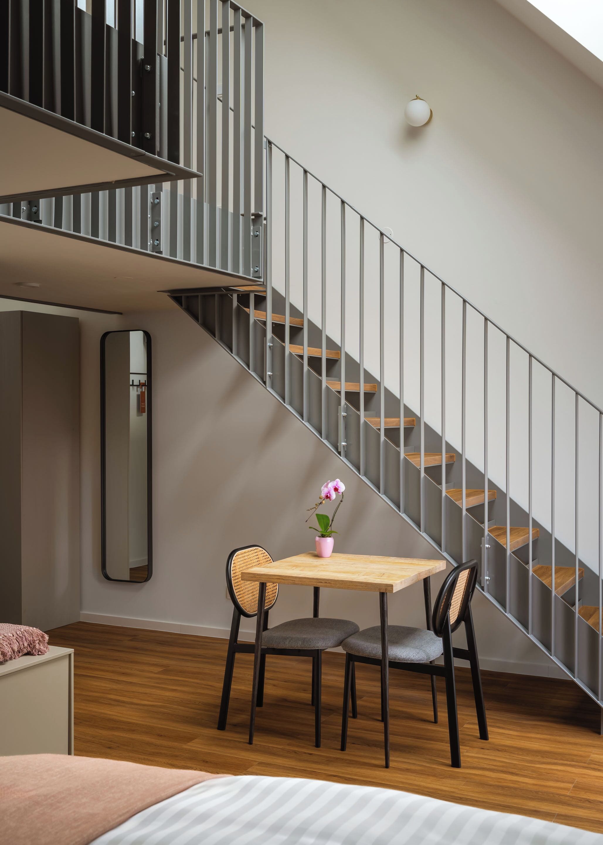Un intérieur moderne avec un escalier, une table à manger entourée de chaises et une petite plante en pot.