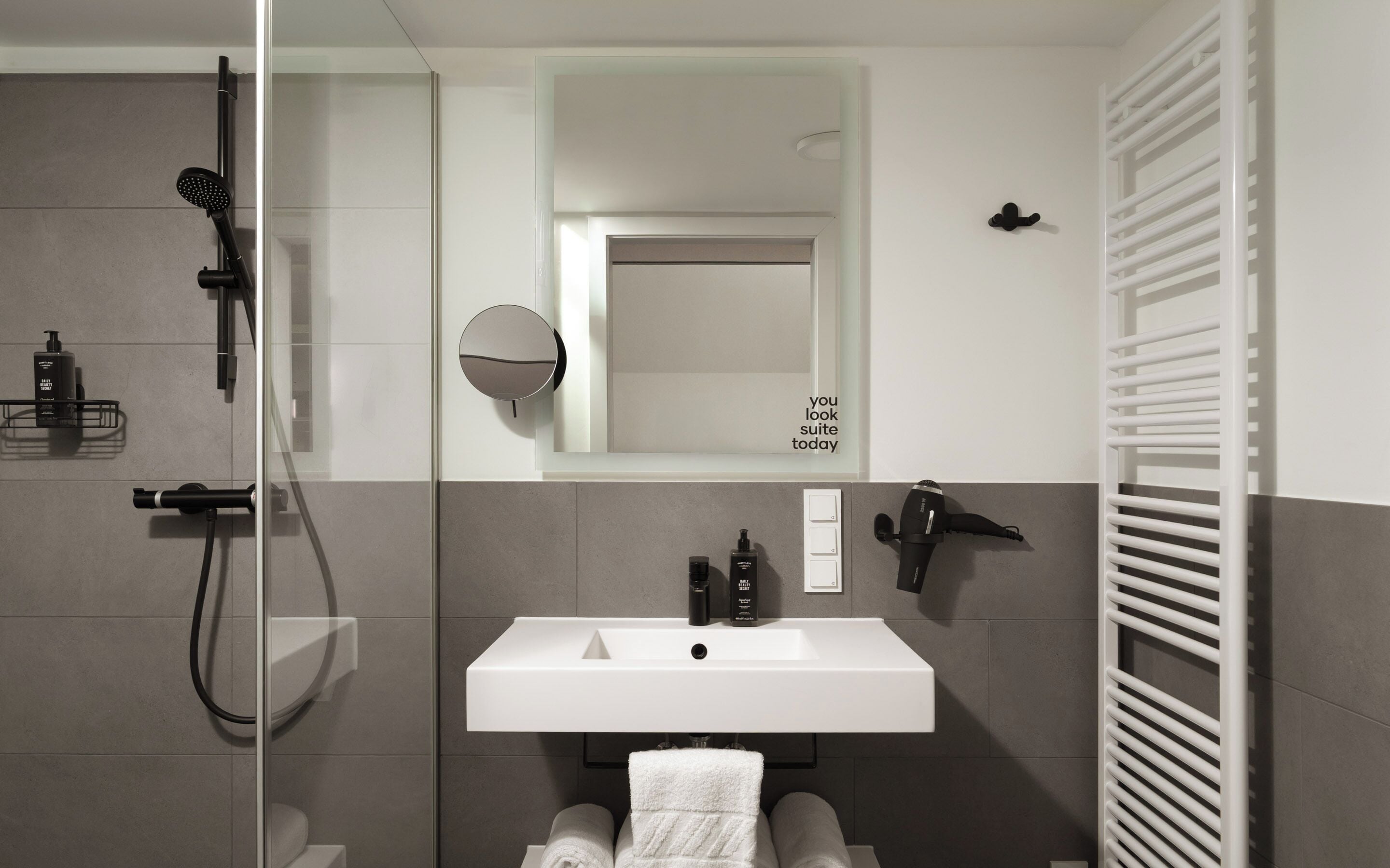 A modern bathroom with a glass shower enclosure, a white sink, and a towel rack.