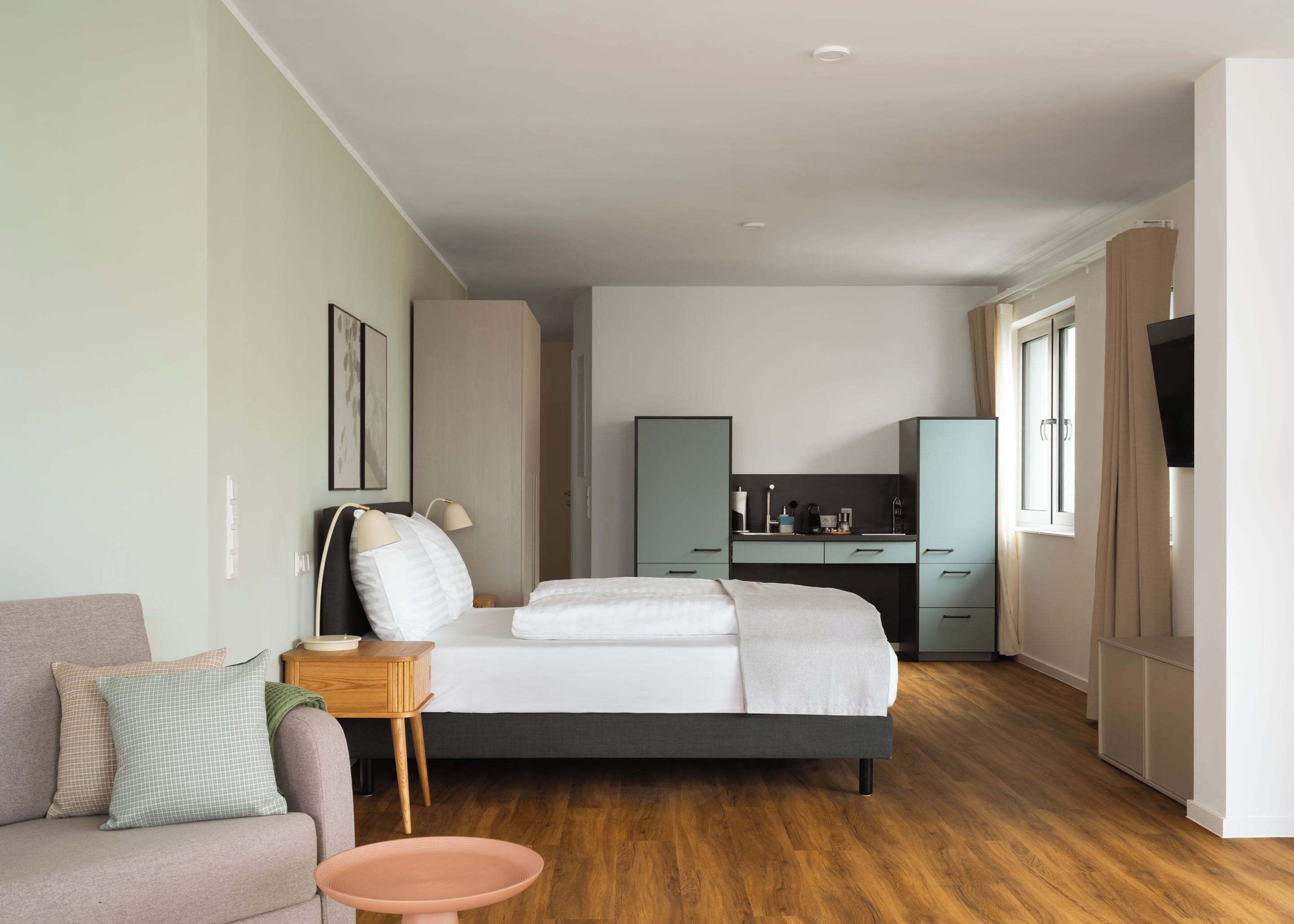 Moderni hotellihuone, jossa on sänky, pieni työpöytä, sohva ja pieni keittiö.