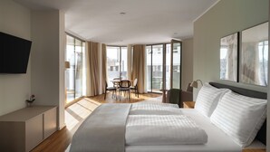 Una habitación de hotel moderna con una cama grande, un área de comedor y un balcón con vistas.