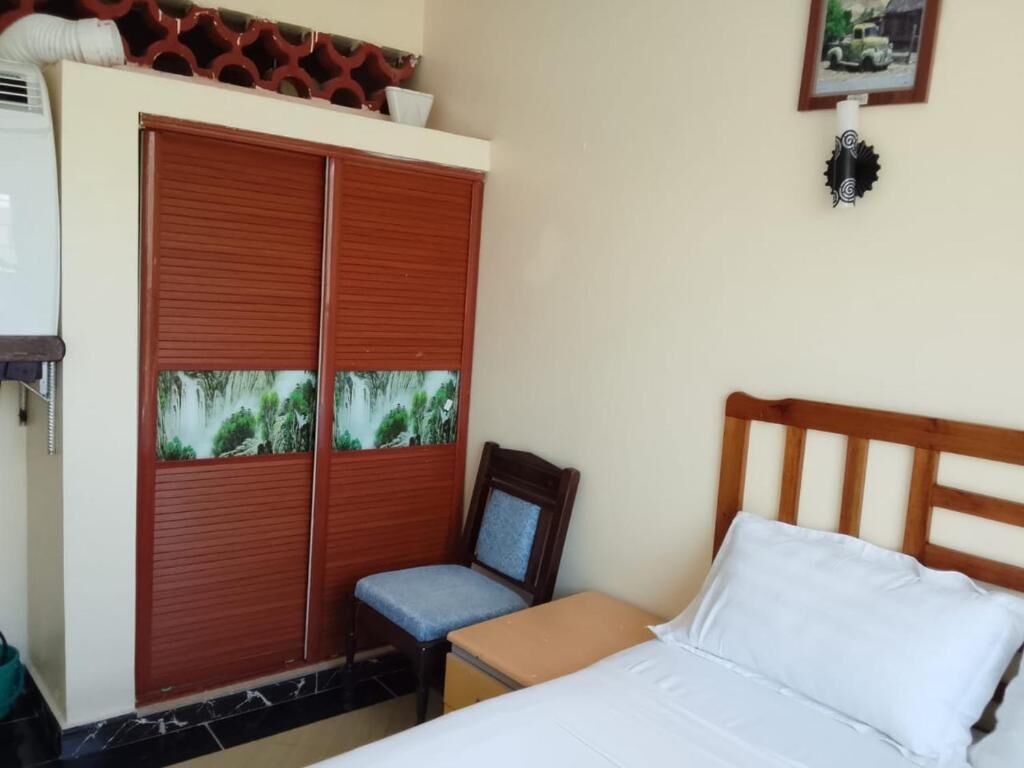 A bedroom with a bed, a wooden headboard, a wardrobe with a view of a forest, a chair, and a small table.